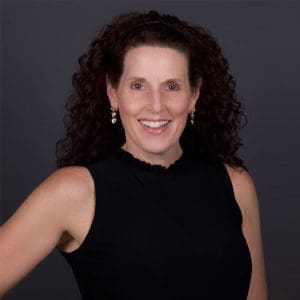 Jill Fritzo in a black sleeveless blouse in front of a dark grey background