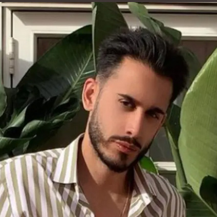 Aasim Khan in a thick-striped button up shirt in front of large foliage